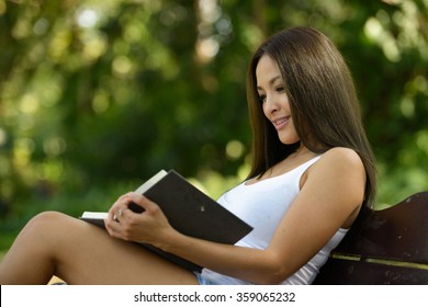 Asian Woman Reading Book Outdoors In Park