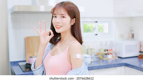 Asian Woman Receiving Coronavirus Vaccine And She Shows Her Arm To You With Ok Gesture In Kitchen At Home