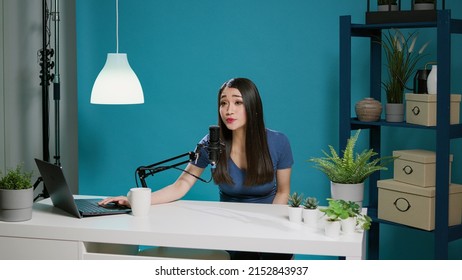 Asian woman recording online podcast with microphone on camera, having conversation with social meida audience. Content creator streaming live discussion in with equipment in studio.