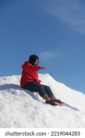 Asian Woman In Red Hoodie Trying To Slide On Snow Mound 