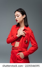 asian woman in red pants and jacket with brooch posing with hand in pocket isolated on grey - Shutterstock ID 2235546595