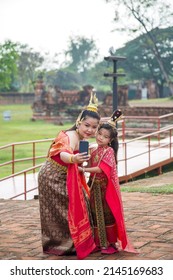 An Asian Woman In A Red Thai Traditional Dress Take A Picture With Her Daughter By Her Phone While Traveling In Ayutthaya