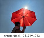 Asian woman with red umbrella walking outdoors in hot weather against cloudless blue sky background. concept of global warming and heat wave in Asia.