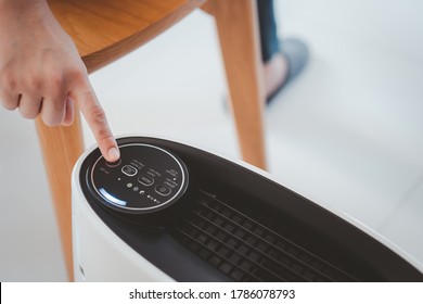 Asian Woman Relaxing In The Living Room While The Modern Portable Air Purifier Working. Woman Using Air Purifier In The Living Room To Purify Or Clean The Polluted Air And Atmosphere.