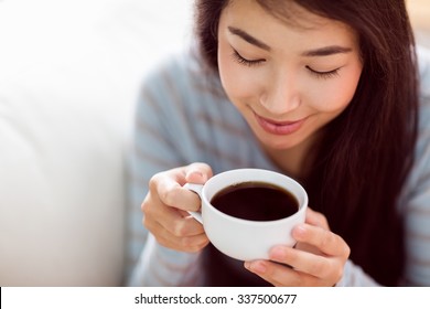 Asian Woman Relaxing On Couch With Coffee At Home In The Living Room