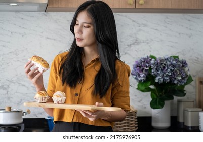 Asian Woman Relishes Deliciously Aromatic Bread, A Snack Just Baked From The Oven In Her Home Kitchen. It's A Hobby Of Making Bread.