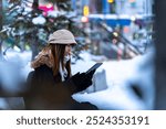 Asian woman remote working on digital tablet during waiting for bus in winter night. Attractive girl enjoy urban outdoor lifestyle travel in the city with using wireless technology and gadget device.