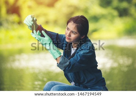 Asian woman researcher black hair in blue jean volunteer charity working checking controlling the quality of water environment with glass tube at green forest near river at ratchaburi thailand.