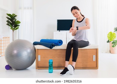 Asian Woman Resting And Using Smart Watch After Play Yoga And Exercise At Home Background With Copy Space.Concept Of Sport Technology To Checking Health Data.