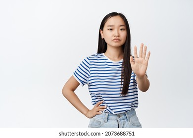 Asian Woman Say No. Teen Girl Extend One Hand, Taboo Refusing Gesture, Stop Sign, Frowning And Looking Serious At Camera, White Background