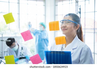 Asian Woman Scientist Microbiology And Chemist Writing Table Of The Elements On Glass Board In Laboratory Room. Science And Medical People Concept 