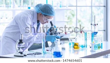 Asian woman scientist, researcher, technician, or student conducted research or experiment by using microscope which is scientific equipment in medical, chemistry or biology laboratory
