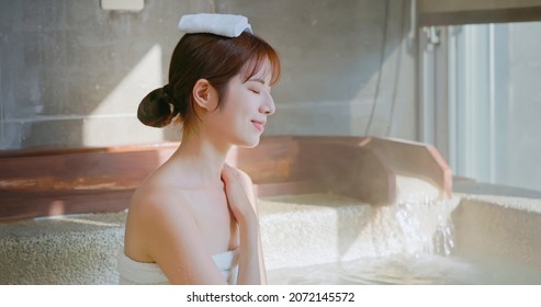 asian woman scoop up the water and pour on her body while sitting in hot spring 
