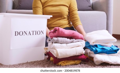 Asian woman selecting clothes for donation and putting them in a box. Concept campaign to donate unused items. - Shutterstock ID 2004819878