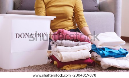 Asian woman selecting clothes for donation and putting them in a box. Concept campaign to donate unused items.