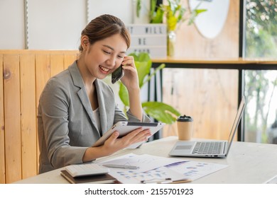 Asian Woman, Self-employed, Focusing On Mobile Phone With The Laptop. Financial Analysis, Graphs, Accounts, Charts, Online Marketing Plans, Working Concepts Based On Coffee Shops Outside The Home.