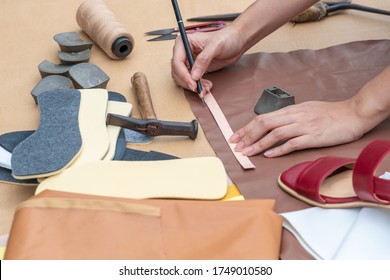 Asian Woman Shoemakers's Hand Drawing Or Drafting Woman Shoes Template For Cutting Leather With Tools And Accessories And Woman Shoes Sample On Table.