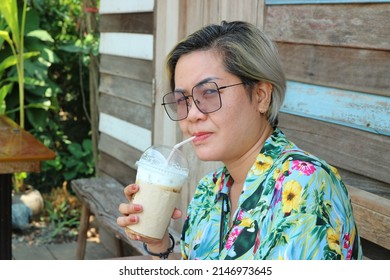 Asian Woman, Short Hair, LGBTQ, Sitting And Drinking Iced Coffee. Relaxing Mood At The Cafe