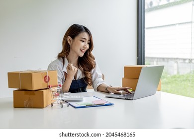 An Asian Woman Showing Joy After Reaching Her Daily Sales Target, She Owns An Online Store, She Packs And Ships Through A Private Transport Company. Online Selling And Online Shopping Concepts.