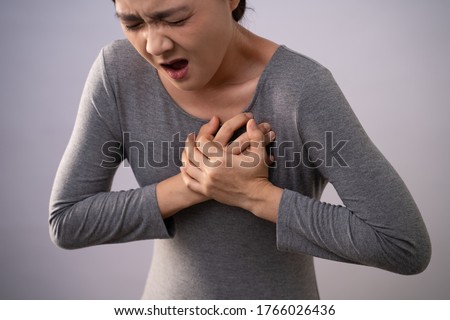Asian woman was sick with chest pain, putting her hands on her chest and standing isolated on background.