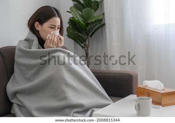 Asian woman sick with fever, runny\
nose and cough at home during the COVID-19\
outbreak.
