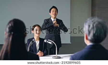 Asian woman and sign language interpreter at press conference.