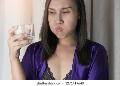 Asian woman in silk nightwear and silk purple robe drinking water against a gray background, People Rinsing And Gargling While Using Mouthwash From A Glass - Dental Healthcare Concepts - Powered by Shutterstock