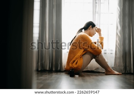 Asian woman sit Depression Dark haired  pensive glance Standing by window and anxiety Copy space. 

