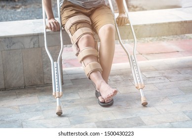 Asian Woman Sit On Bench With Walking Stick And Knee Brace Support Surgery Right  Knee In Recovery Time.