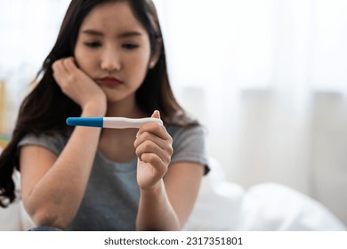 Asian woman sitting bed feeling disappointed when see the pregnancy test result. Woman feels worry and not ready to be a mother. Man feeling stress about the future kid holding head. - Powered by Shutterstock