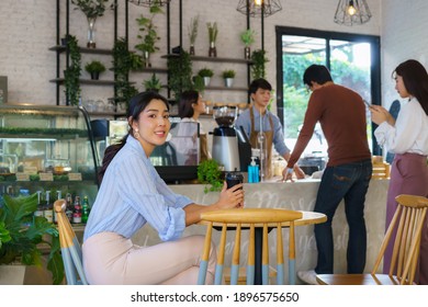 Asian Woman Sitting In Cafe And Feeling Happy While She Drink Coffee And Another People Queue Order Beverage With Barista .
