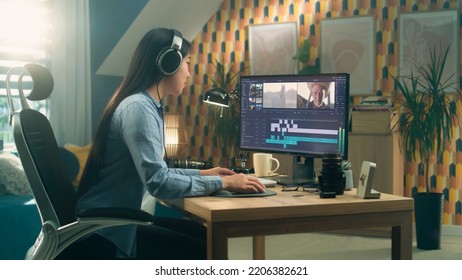 Asian Woman Sitting At The Desk In Headphones At Home Office And Editing Video For Blog In Professional Program On Computer. Freelance