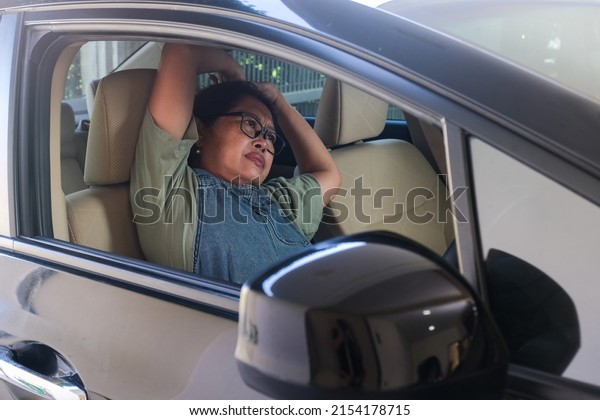 An Asian woman sitting in the\
driver\'s seat tries to get rid of sleepiness by\
stretching.