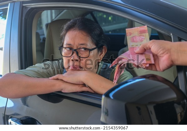 An Asian woman sitting in the driver\'s\
seat glanced and showed a disapproving face when the money given to\
her was not enough to buy what she\
wanted.