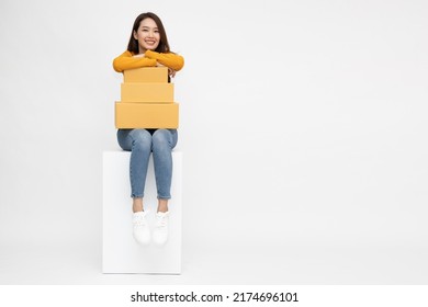 Asian Woman Sitting And Holding Package Parcel Box Isolated On White Background, Delivery Courier And Shipping Service Concept, Full Body Composition