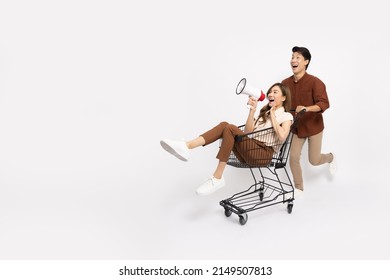 Asian woman sitting inside of shopping trolley and holding megaphone and Asian man pushing shopping cart isolated on white background, Announce sale concept