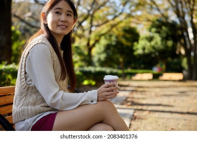 Asian Woman Sitting On A Bench With A Coffee Cup