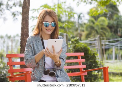 Asian Woman Sitting On A Bench Watching Tablet