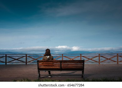 Asian Woman Is Sitting On The Bench With The Blue Sky Background.