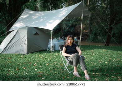 Asian woman sitting on a lawn chair rest on vacation Female tourists like to travel and go camping. pitch a tent and sleep in the natural forest - Shutterstock ID 2188617791