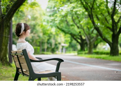 Asian Woman Sitting On A Park Bench