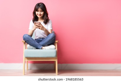 Asian woman sitting on sofa using her phone with a happy expression