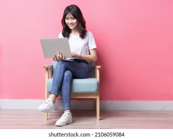 Asian Woman Sitting On Sofa Using Laptop With Happy Expression	