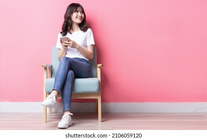 Asian Woman Sitting On Sofa Using Her Phone With A Happy Expression	