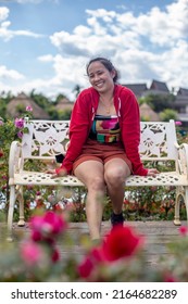 Asian Woman Sitting On White Iron Bench In Park