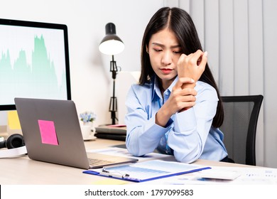 An Asian woman is sitting overtime with her laptop and her wrist aches while working at the office. - Powered by Shutterstock