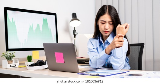 An Asian woman is sitting overtime with her laptop and her wrist aches while working at the office.