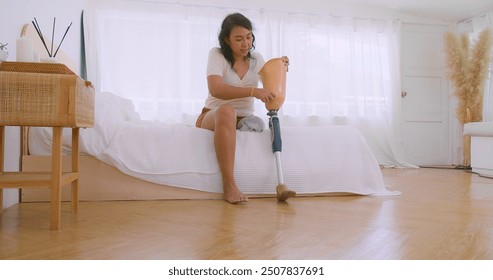 Asian Woman Sitting relaxing on Bed and adjusting put on her Prosthetic Leg after wake up everyday in Bright Bedroom, Life difficulties of amputee, Amputee lifestyle, Leg prosthetic equipment - Powered by Shutterstock