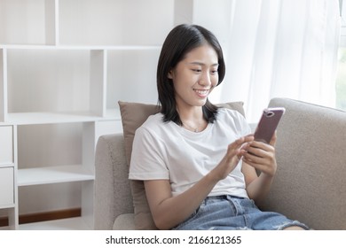 Asian woman sitting with smart phone on sofa in living room, Looking at tablet screen, Relaxing at home, Working through the Internet communication system, Happy working lifestyle. - Shutterstock ID 2166121365