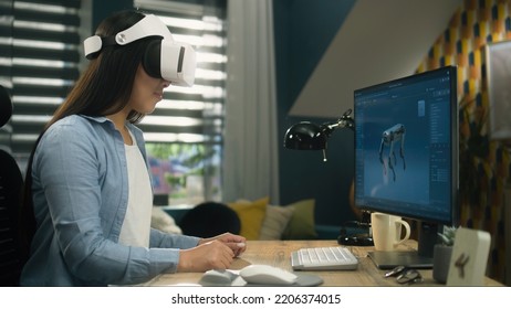 Asian Woman Sitting At The Table At Home Office And Using VR Headset To Work On 3D Modeling Project On Personal Computer. Virtual Reality. Metaverse